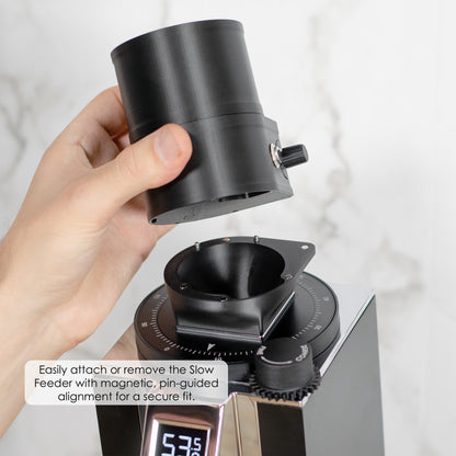 Close-up of a person holding the ARO Slow Feeder above a grinder, showing the magnetic, pin-guided alignment system for easy attachment and removal.