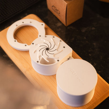 White ARO Espresso slow feeder shown disassembled on a wooden board with its components laid out.