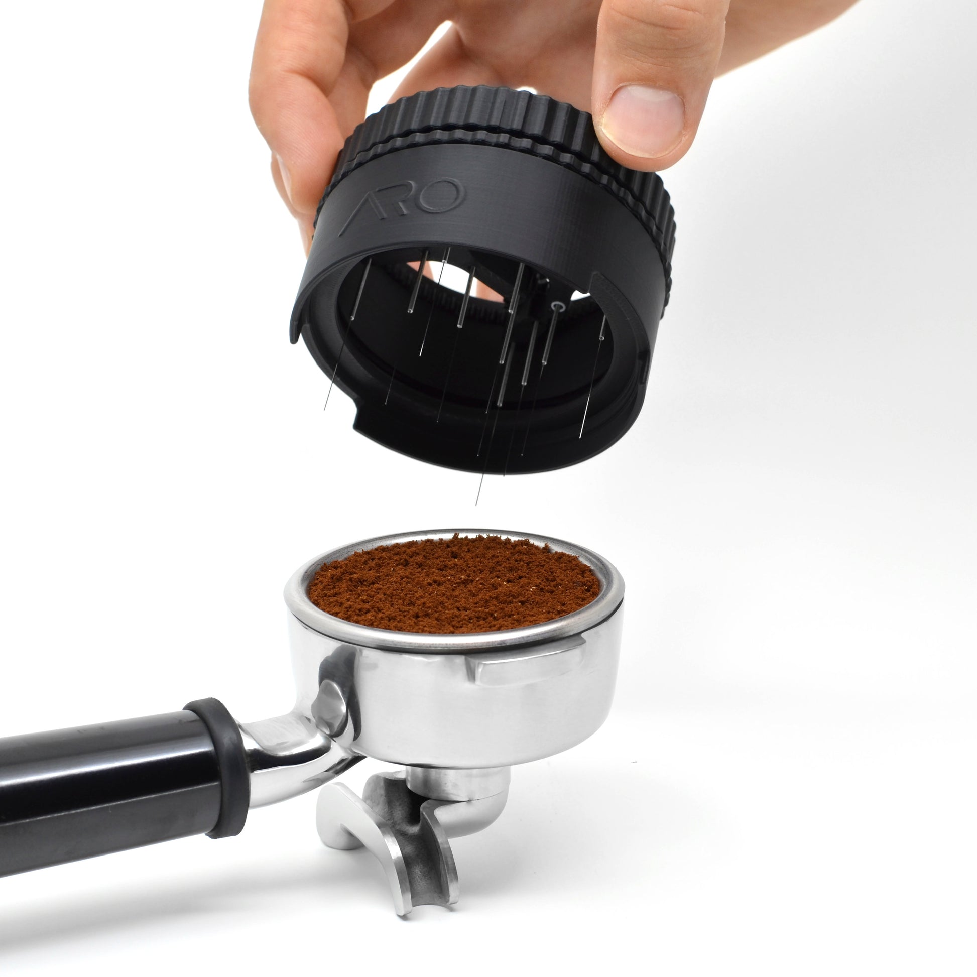 A hand removing a spinning WDT tool from a portafilter with espresso grounds in it.